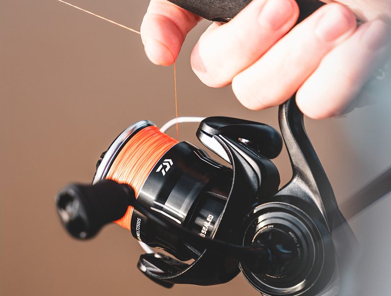 24 TD Black MQ spinning reel spooled with orange braid, held on a rod